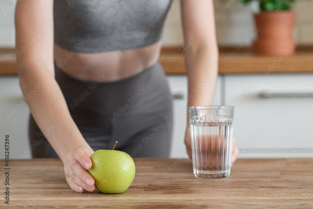 Unrecognisable fitness girl holding green apple and glass of water in her hand. Correct and dietary nutrition concept Unrecognisable fitness girl holding green apple and glass of water in her hand. Correct and dietary nutrition concept