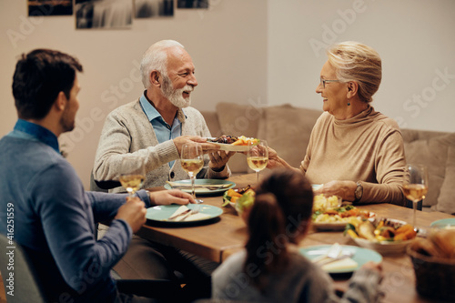 Happy senior couple passing food during family lunch at dining table.