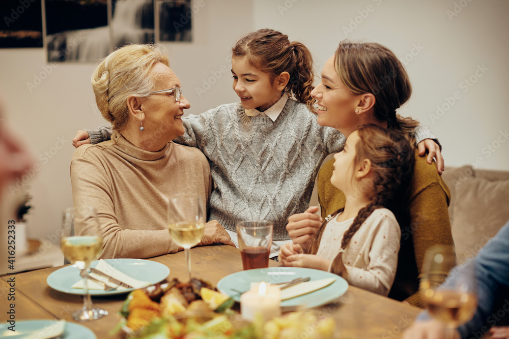 Happy senior woman talking with her granddaughters and daughter in dining room.