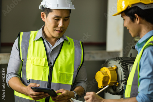 Senior and junior engineers talking together with intimated manner beside the machine in factory. Concept for good teamwork and unity of colleauges photo