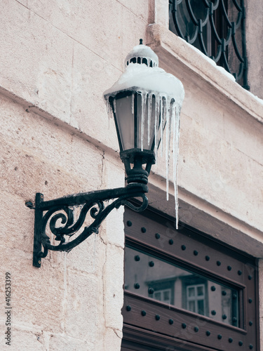 Snow covered street lamp or light post lantern on an old building with icicles. Romantic urban winter with a lantern