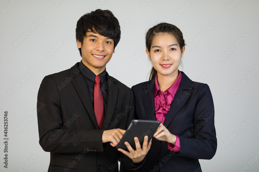 Asian man and woman businesspeople in formal suit standing together and holding tablet computer and smile to camera with self-confidence Asian man and woman businesspeople in formal suit standing together and holding tablet computer and smile to camera with self-confidence