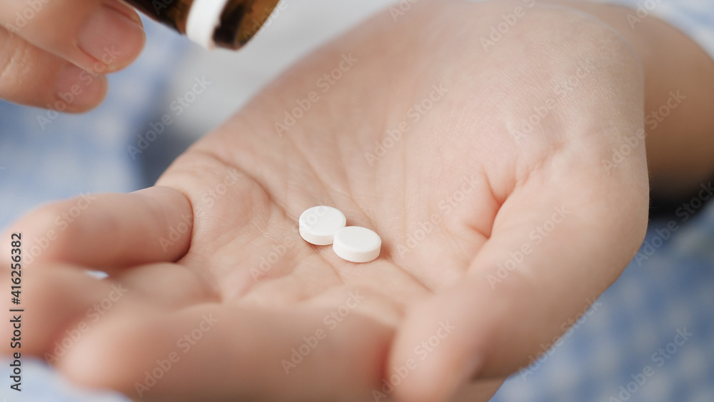 Two average size white round pills fall into palm of hand from pill bottle. Close-up, front view, center composition Two average size white round pills fall into palm of hand from pill bottle. Close-up, front view, center composition