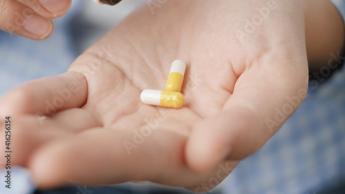 Two big white-yellow cylindrical capsule pills fall into palm of hand from pill bottle. Close-up, front view, center composition