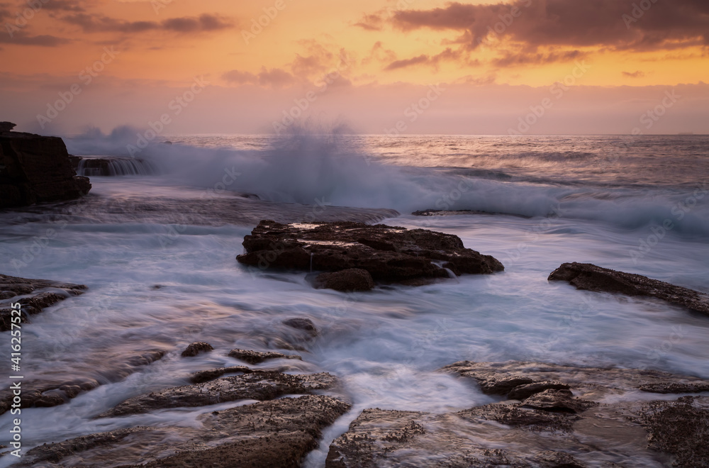 Fototapeta premium Coastal sunrise waves crashing onto rocks
