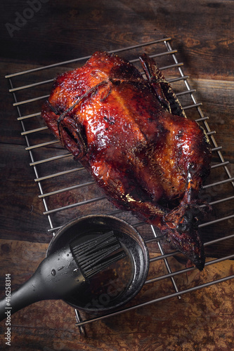 Whole duck stuffed glazed in honey sauce on BBQ grate on wooden background. Festive menu.