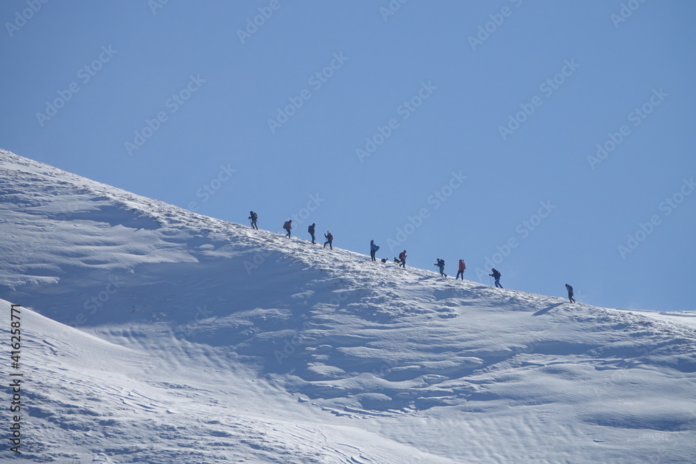 Climb a mountain. A group of hikers climbs the snow-capped peak of Mt. Hiking group in winter snowy mountains. Climbers walking on climbing the mountain range.