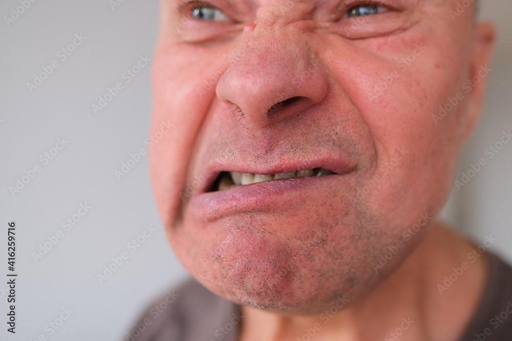Obraz premium face of a European old man close-up, wrinkles on the aging skin, bares his teeth, makes grimaces, opening his mouth, the concept of mental health, cosmetology, age-related changes