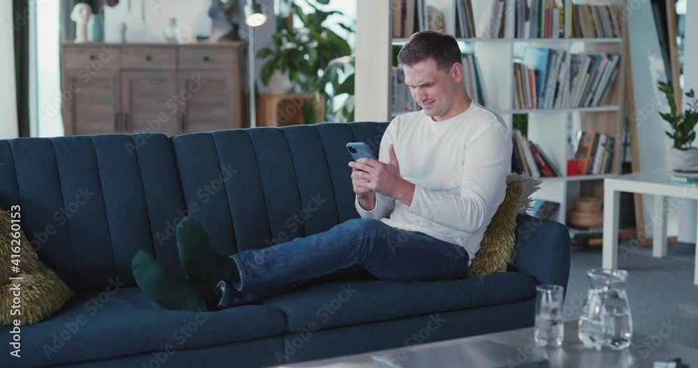 Young manusing smartphone in living room casual modern apartment texting messages netowkring on social media pps indoors. Young manusing smartphone in living room casual modern apartment texting messages netowkring on social media pps indoors.