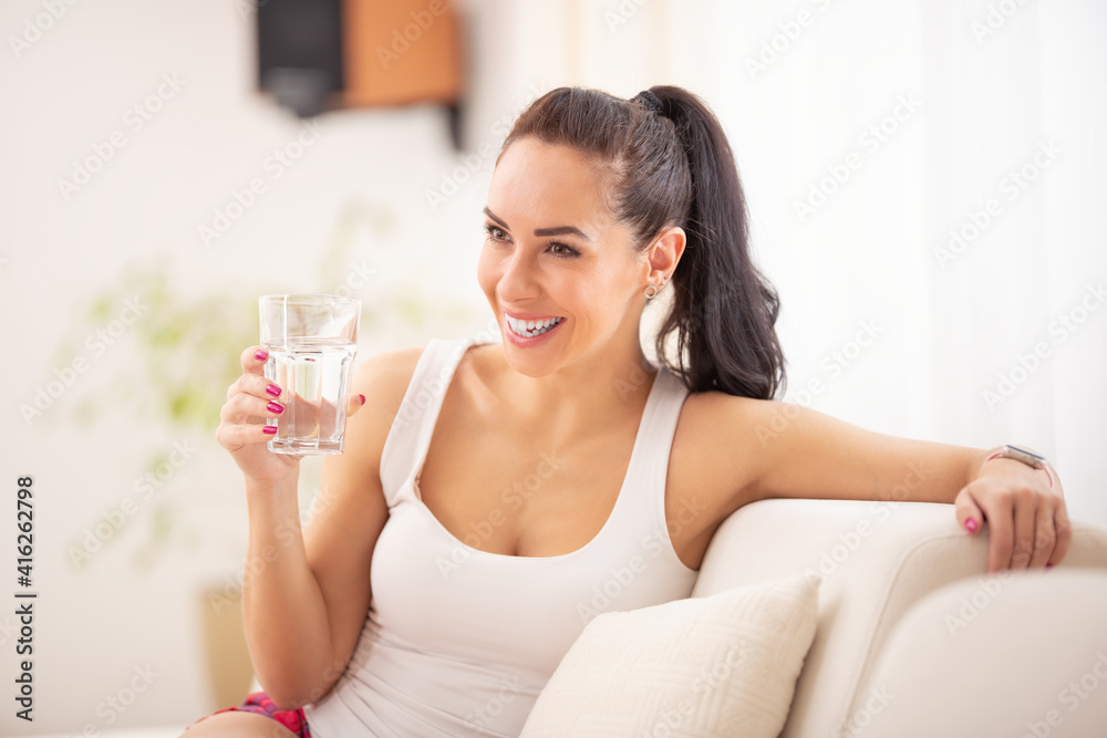 Beautiful woman laughs while sitting on a sofa drinking a glass of water Beautiful woman laughs while sitting on a sofa drinking a glass of water
