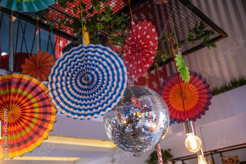 A room ceiling decorated for birthday party with discoball, colorful balloons and ribbons and other multicoloured different elements. Festive decoration of the room.