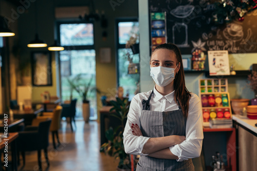 waitress standing crossed arms in restaurant, She has protective face mask due covid-19