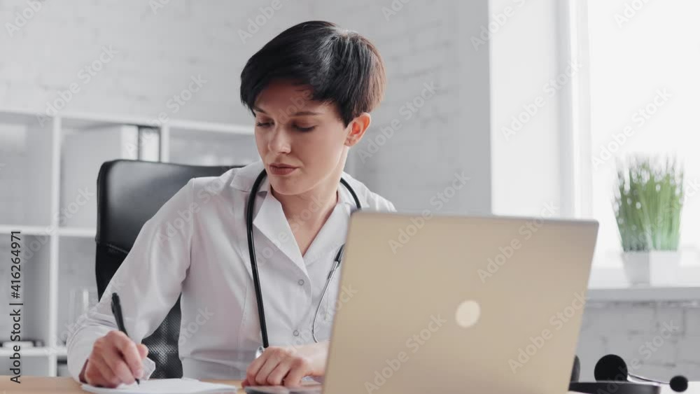 Female doctor wearing white coat consulting patient remote online using headset and web camera on laptop. Giving recommendations treatment prescription.Telemedicine,remote healthcare services concept Female doctor wearing white coat consulting patient remote online using headset and web camera on laptop. Giving recommendations treatment prescription.Telemedicine,remote healthcare services concept