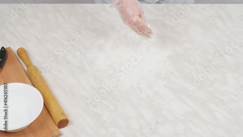 Close-up of a woman's hand sprinkles the table with flour and lays down the dough.