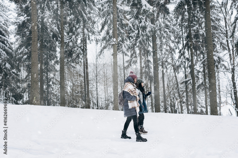 Two active young tourists in warm winter clothes are walking on the background of a beautiful snow-covered landscape.Hiking.Individual adventures.Local travel