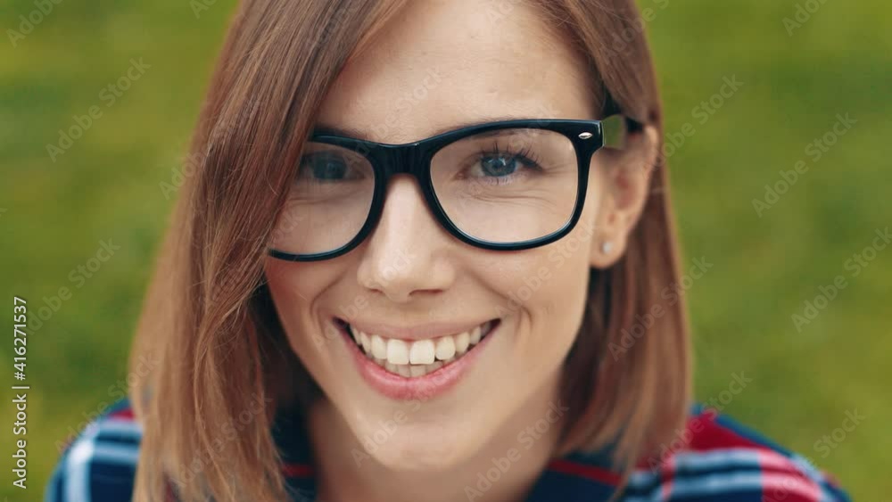 Close up portrait of young beautiful blonde woman with glasses sitting on background of green grass and smiling looking at camera. Close up portrait of young beautiful blonde woman with glasses sitting on background of green grass and smiling looking at camera.
