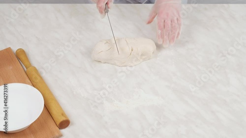 Close-up, female hands in gloves crumple the dough and cut it with a knife.