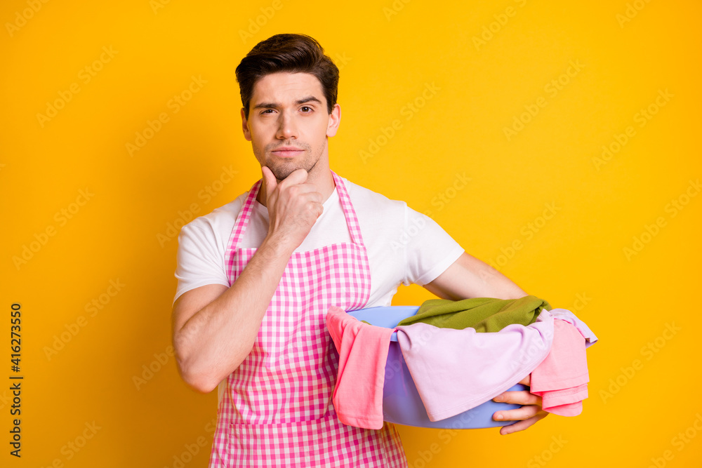 Photo of young serious thoughtful minded man thinking hold basin with dirty clothes isolated on yellow color background