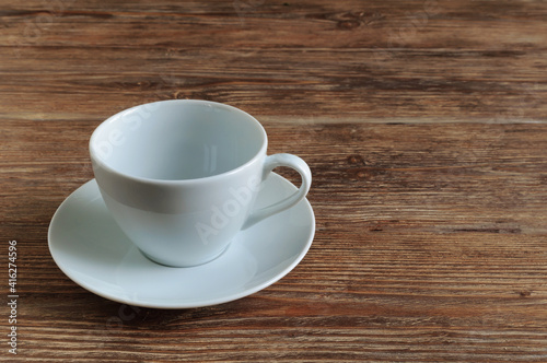 Empty white porcelain cup and saucer on wooden table. Copy space