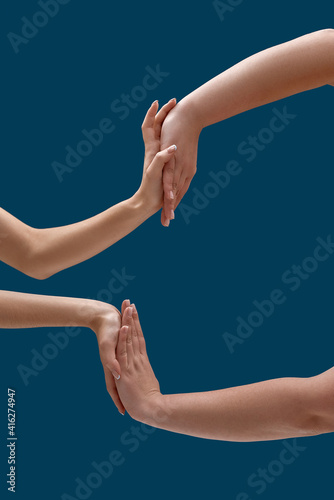 Close up of two women holding or measuring hands, touching each other palms isolated over blue background