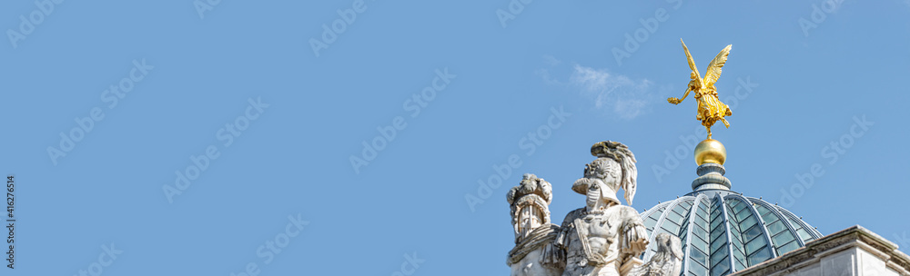 Obraz premium Banner with old statue of golden angel as warrior and defender at the dome top in historical downtown of Dresden, Germany, with copy space and blue sky background.