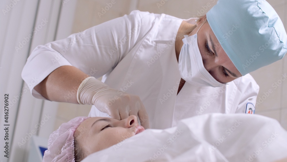 Fototapeta premium Cosmetologist in protective mask making treatment procedure to patient. Beautician makes injections in the woman's face. Mesotherapy. Doctor in medical gloves put injections in female face.