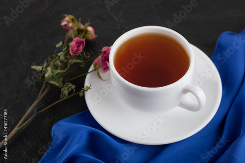 Dried roses with a cup of hot tea on a black background