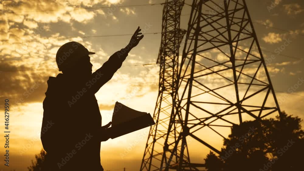 silhouette of an electrician engineer working next to an electrical support tower energy. electricity sunset high voltage tower support. electrical engineer inspect voltage electricity pylon