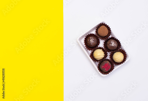 Chocolate cheese truffles, homemade chocolate. Delicious chocolate candies. Group of sweet chocolate truffles on yellow, white background © Inna