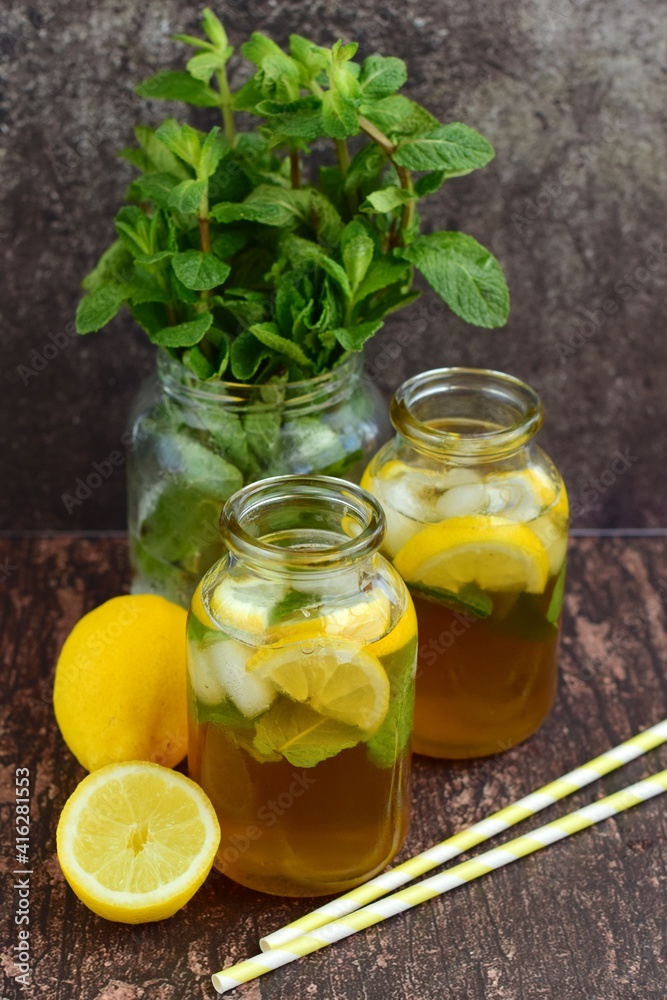Iced lemon tea with lemon slices and mint leaves and ice cubes on rustic background Iced lemon tea with lemon slices and mint leaves and ice cubes on rustic background