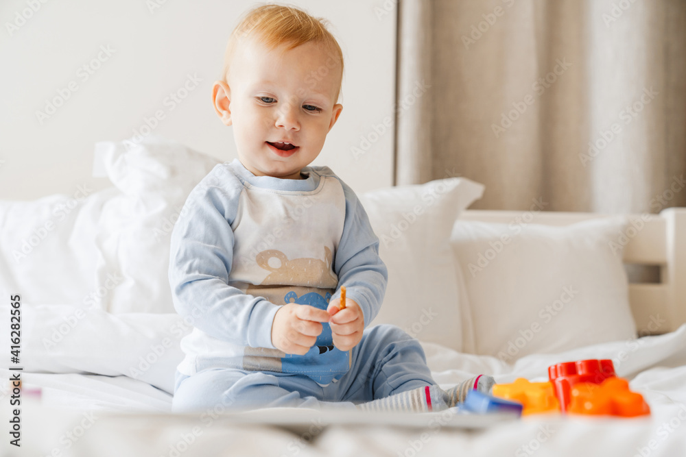 Pleased blonde baby boy looking at tablet computer while playing on bed Pleased blonde baby boy looking at tablet computer while playing on bed