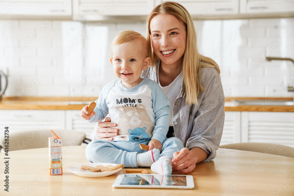 Happy beautiful woman using tablet computer while feeding her baby son Happy beautiful woman using tablet computer while feeding her baby son