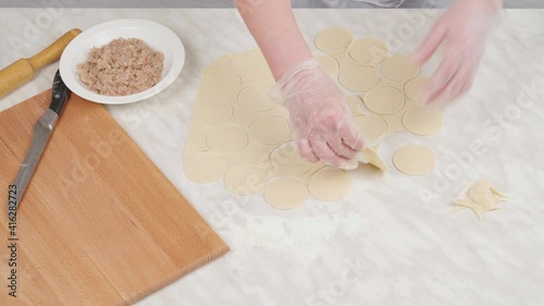 A woman cuts circles out of raw dough with a mold and removes excess dough. Preparation for homemade dumplings.