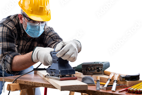 Carpenter worker at work isolated on white background, wears helmet, goggles, leather gloves and surgical mask to prevent coronavirus infection. Preventing Pandemic Covid-19 at the workplace.