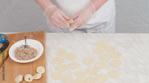 The woman takes the minced pork from the bowl with a spoon and puts it on the dough circle, pinching the edges. Making homemade dumplings. Traditional Russian food.
