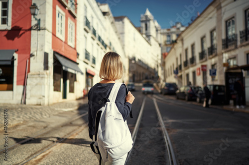 Traveling by Portugal. Happy young woman with rucksack walking by streets in Lisbon.