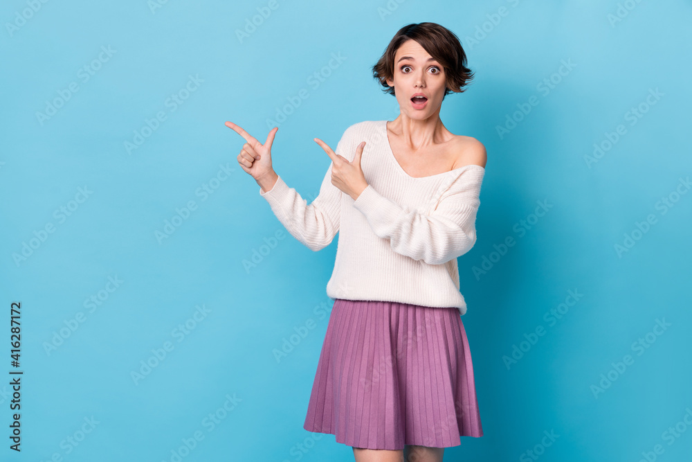 Photo portrait of amazed woman pointing two fingers at blank space isolated on pastel blue colored background Photo portrait of amazed woman pointing two fingers at blank space isolated on pastel blue colored background