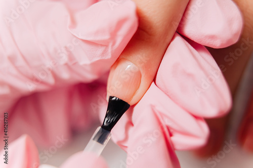 Manicure process. The master paints the nails with transparent varnish