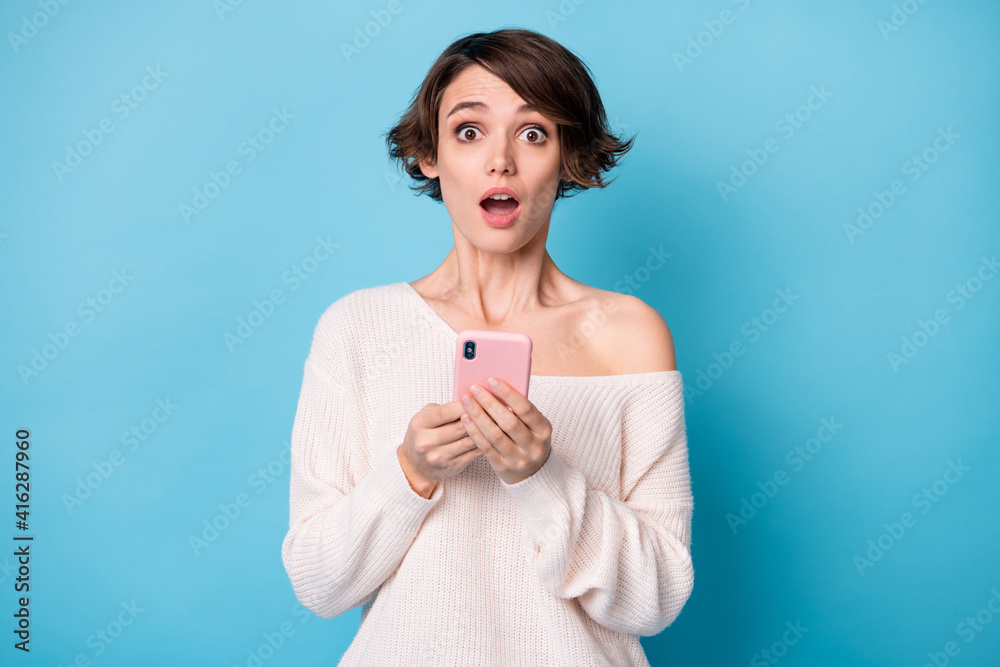 Photo of young beautiful shocked surprised amazed girl see bad comment use phone isolated on blue color background Photo of young beautiful shocked surprised amazed girl see bad comment use phone isolated on blue color background
