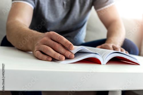 Caucasian man reading a book at home. Cropped shot of an unidentifiable man reading a book. Young man reading book while sitting on the couch. Close up picture of men hand opening book selective focus