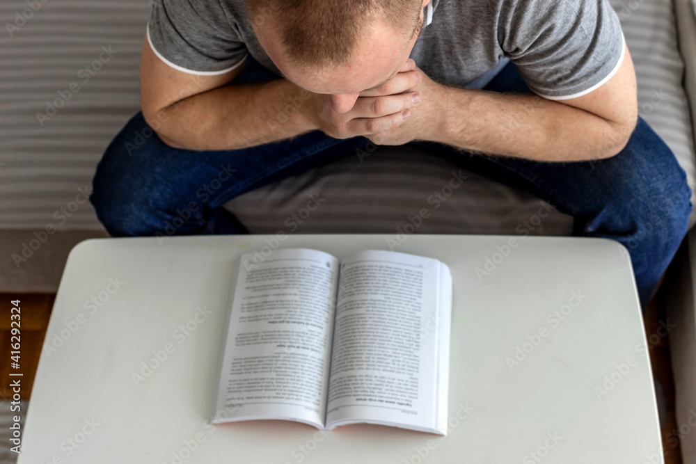 Young man sitting in the lounge and reading a book. Adult Caucasian man sitting on sofa bed at home reading a book, study, learning alone during the quarantine lockdown. Education, lifestyle concept. Young man sitting in the lounge and reading a book. Adult Caucasian man sitting on sofa bed at home reading a book, study, learning alone during the quarantine lockdown. Education, lifestyle concept.
