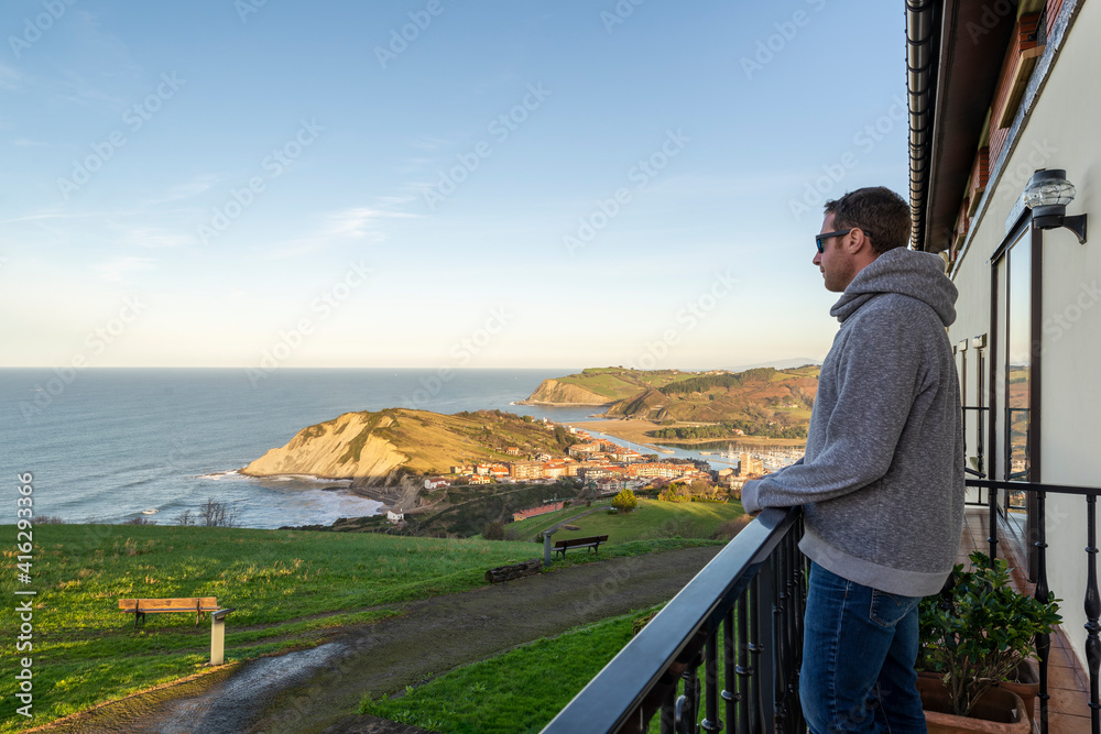 Man in casual clothing standing on a balcony and looking at a sunset over zumaia, Spain. Man in casual clothing standing on a balcony and looking at a sunset over zumaia, Spain.