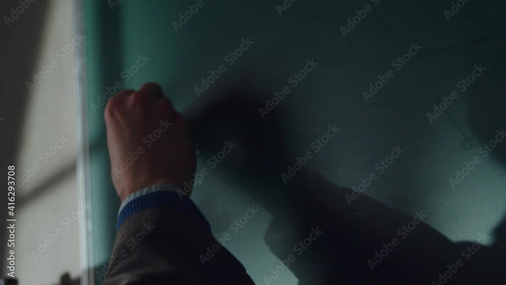 Young teacher man writes mathematical formulas using chalk on a green school chalkboard Young teacher man writes mathematical formulas using chalk on a green school chalkboard