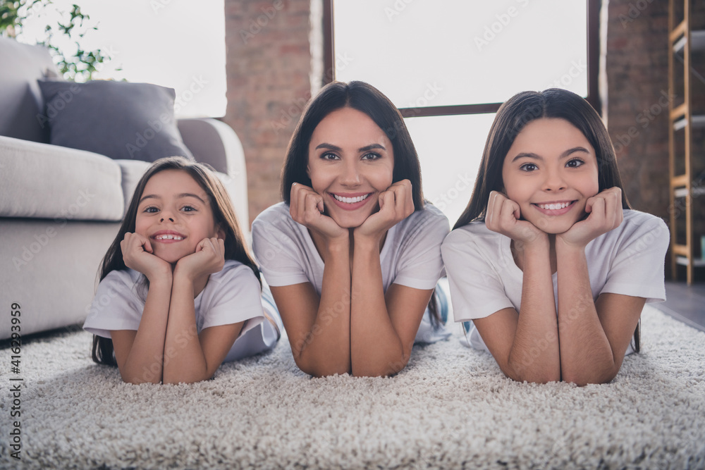 Photo of charming cheerful lady cute little girls lying on floors arms on cheeks toothy smile look camera have fun indoors Photo of charming cheerful lady cute little girls lying on floors arms on cheeks toothy smile look camera have fun indoors