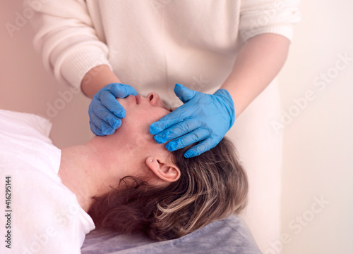 Cosmetologist's hands in gloves on a woman's face, buccal massage and lifting facial skin