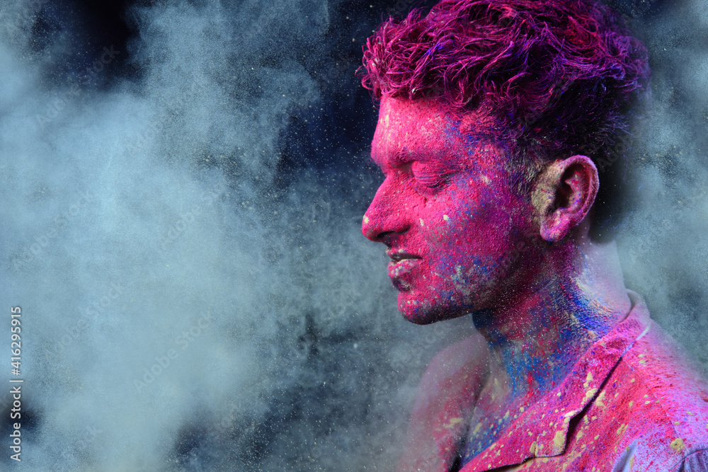 Portrait of a young man plays with Holi colours. Concept for Indian festival Holi	