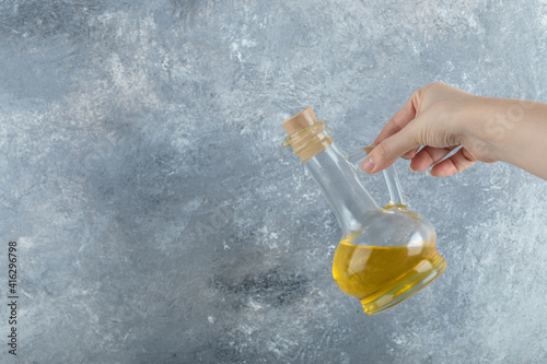 Female hand holding bottle of vegetable oil on grey background photo