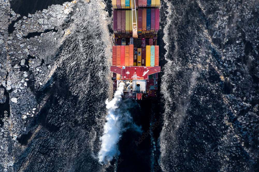 Cargo ship driving through frozen sea with colorful containers. Dark waters with ice blocks floating in sea.