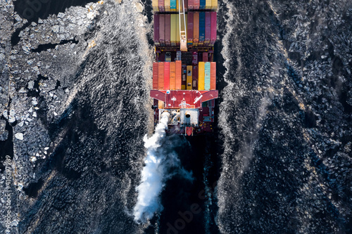 Obraz na płótnie Cargo ship driving through frozen sea with colorful containers. Dark waters with ice blocks floating in sea. w salonie