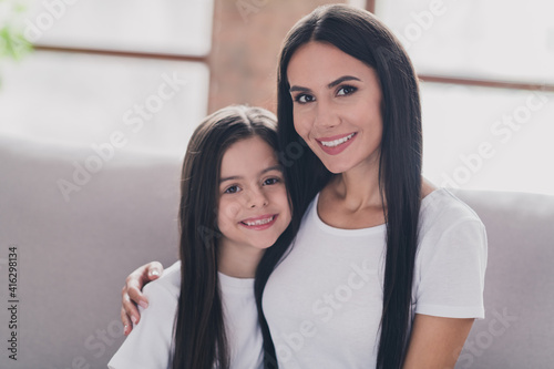 Portrait of beautiful tender gentle cheerful girls best friends sitting on divan mom hugging adopted foster kid rest at house loft flat indoors
